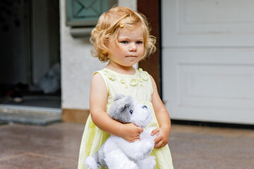 Little toddler girl playing with soft toy dog. Cute baby child holding toy and plays outdoors.