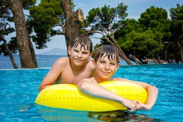 Two kids boys having fun on inflatable rubber rings in outdoor pool. Summer holiday. Summertime...