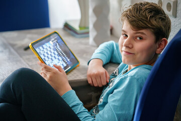 Caucasian teenager boy playing chess on tablet. Kid child plays game with virtual opponent.
