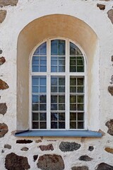 Old stone wall with white painted frame window with an arch.