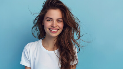 Pretty young smiling woman with dark hair on a blue background with copy space. Cute girl in a simple white T-shirt.