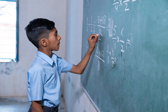 Happy Indian rural school boy write on chalkboard or blackboard in classroom, Education concept.