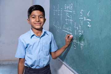Happy Indian rural school boy write on chalkboard or blackboard in classroom, Education concept.