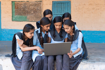 Group of rural school girls in uniform sitting in school corridor working on laptop - concept of digital education