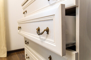 A white dresser with a gold handle and a drawer that is open