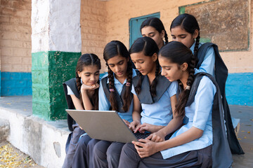 Group of rural school girls in uniform sitting in school corridor working on laptop - concept of...