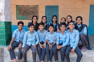 Group of rural indian school students sitting together in blue school uniform looking at camera
