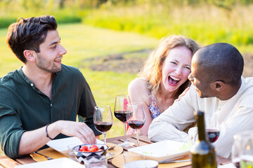 Amidst the golden hour's glow, a trio of friends shares a hearty laugh over a table of wine and...