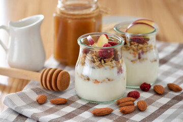 Crunchy granola with yogurt, apple, nuts and honey in glass jars on wooden table. Healthy breakfast concept. - 755642805