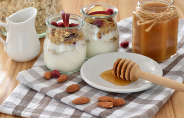 Crunchy granola with yogurt, apple, nuts and honey in glass jars on wooden table. Healthy breakfast concept. - 755642834