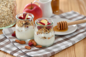 Crunchy granola with yogurt, apple, nuts and honey in glass jars on wooden table. Healthy breakfast concept. - 755642838
