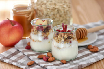 Crunchy granola with yogurt, apple, nuts and honey in glass jars on wooden table. Healthy breakfast concept. - 755642848