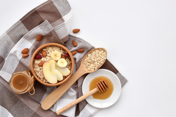Oatmeal in a wooden bowl with almonds and pieces of apple ready to cook, honey, scattered oat flakes and spoon on white background. View from above. Place for text - 755642871