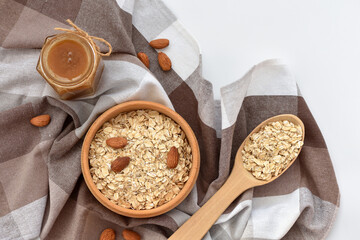 Oatmeal in a wooden bowl with almonds, a jar of honey and with spoon full of oatmeal on white background. View from above. - 755642889