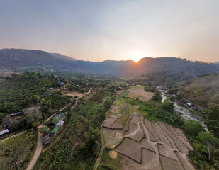High-angle landscape, rice fields in the middle of mountains with a river flowing through. Cold Sunset During the summer there is less water in the river. View from the drone aircraft.