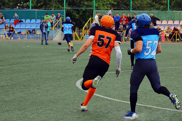 American football players in blue and black uniforms with number 52 runs after an opponent in orange and black uniforms with number 57	
