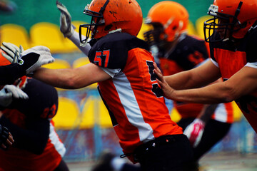 American football players in black and orange uniforms push each other	
