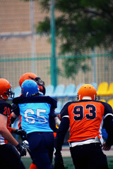 An American football player in an orange and black uniform with the number 93 runs next to a football player in a blue and black uniform with the number 65	
