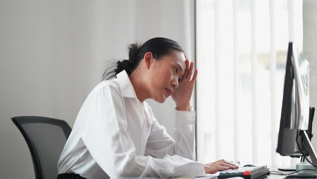 Asian businesswoman working on a computer, feeling tired and frustrated with unresolved work issues at her office. Seeking solutions and striving for improvement