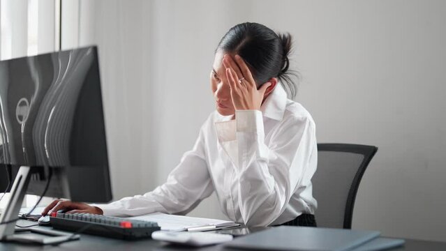 Asian businesswoman working on a computer, feeling tired and frustrated with unresolved work issues at her office. Seeking solutions and striving for improvement