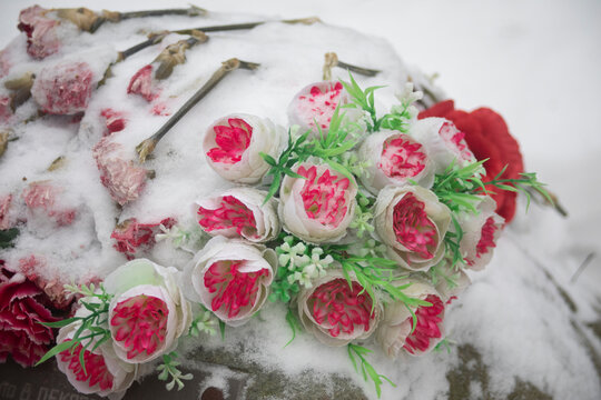 Flowers on the grave. Artificial flowers at the cemetery. Snow on the buds.