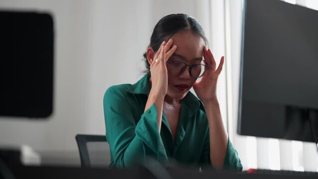 Asian businesswoman working on a computer, feeling tired and frustrated with unresolved work issues at her office. Seeking solutions and striving for improvement