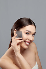 Beautiful woman using facial oil blotting paper. Photo of woman with perfect makeup on gray background. Beauty concept. Cosmetology, cosmetics. Facial treatment