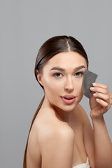 Skin Care. Woman removing oil from face using blotting papers. Closeup Portrait Of Beautiful Healthy Girl With Nude Makeup. Perfect Soft Skin With Oil Absorbing Tissue Sheets. Beauty Concept