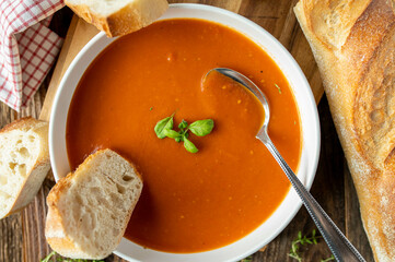 Homemade tomato soup with baguette on a deep plate with spoon