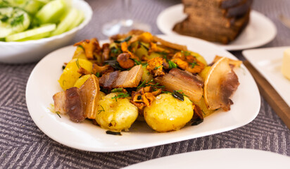 Baked potatoes with chanterelles and bacon served with herbs on white plate