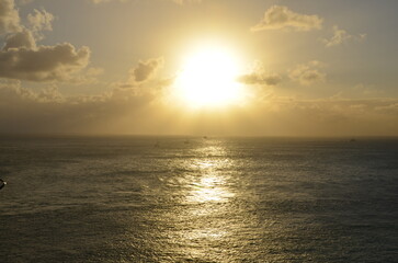 Obraz premium Golden sunset at sea, sailing boat on horizon, reflections of sunrays, sunset sky with clouds