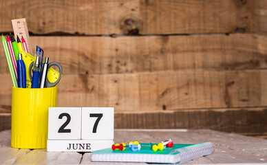 June calendar background with number  27. Stationery pens and pencils in a case on a wooden vintage...