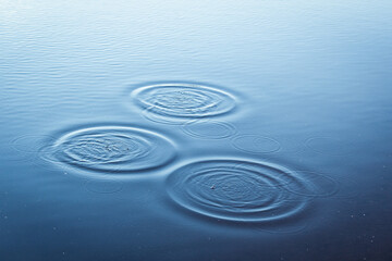 Round droplets of water over circles on the lake. Water drop, whirl and splash.Phone and laptop wallpaper. Close Up water rings affect the surface.