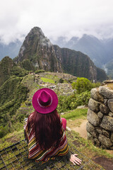 Fototapeta na wymiar A female tourist in a hat and a Peruvian poncho looks at Machu Picchu. Cusco. Peru