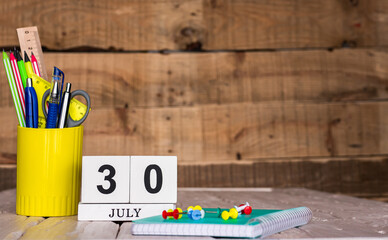 July calendar background with number  30. Stationery pens and pencils in a case on a wooden vintage background. Copy space notepad with pencils and calendar. Planner place for text.