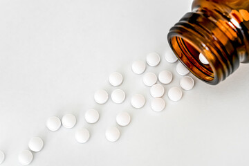 Medicine Close-Up: White Pills and Brown Vial Arranged on White Table, Close-Up, Flat Lay, Top View, Copy Space
