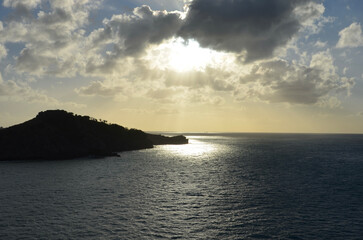 Fototapeta premium Sunset at sea, reflections of sunrays on rippled water surface, clouds, part of an island