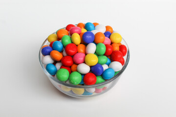 Biscuit balls coated by colorful chocolate. On transparent glass bowl. Isolated on white background