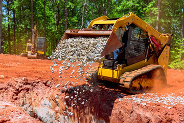 Unloading gravel with an excavator bucket skid steer loader during construction project