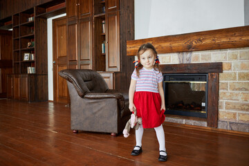 Little girl stands near fireplace holding soft toy in hand - Powered by Adobe