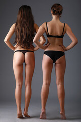 Two pretty slim woman in underwear pose in grey studio, back view
