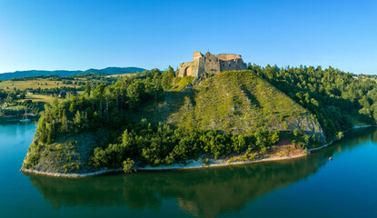 Ruins of medieval castle in Czorsztyn, Poland. Aerial panorama in summer in sunset light. Artificial Czorsztyn lake on Dunajec River. Water reflection and a small tourist boat - 755688659