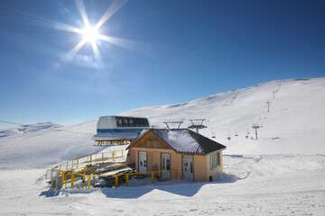 Small cottage. sun and modern ropeway in snowy mountains at winter day