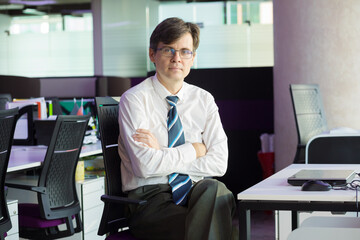 Handsome man in tie and glasses sits at table with laptop in modern office