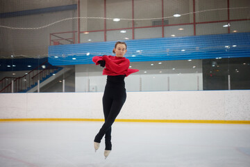 Young slim dancing woman during jump on skate in indoor ice rink