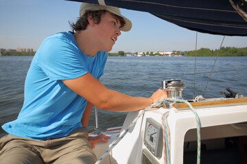 Boy teenager in cap sails on yacht on river at summer sunny day
