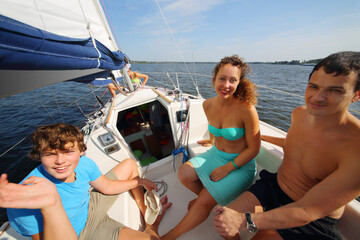Father, mother and son sail on yacht on river at sunny day