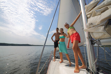 Father, mother and happy daughter sail on white yacht on river at summer sunny day