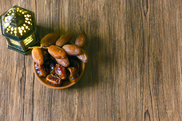 top view of dried dates served on a wooden bowl and a lantern with Arabic calligraphy meaning 