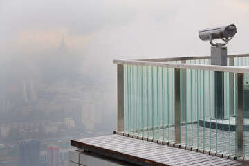 Binoculars on viewing platform on overcast day and buildings in fog , focus on fence